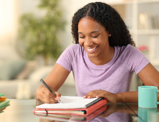 Mulher negra sorrindo ao fazer redação em casa